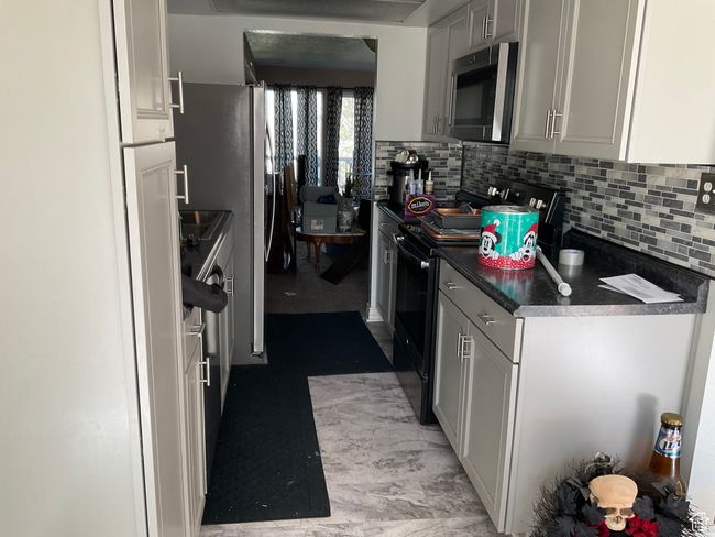 Kitchen with stainless steel microwave, dark countertops, decorative backsplash, and black electric range | Image 11