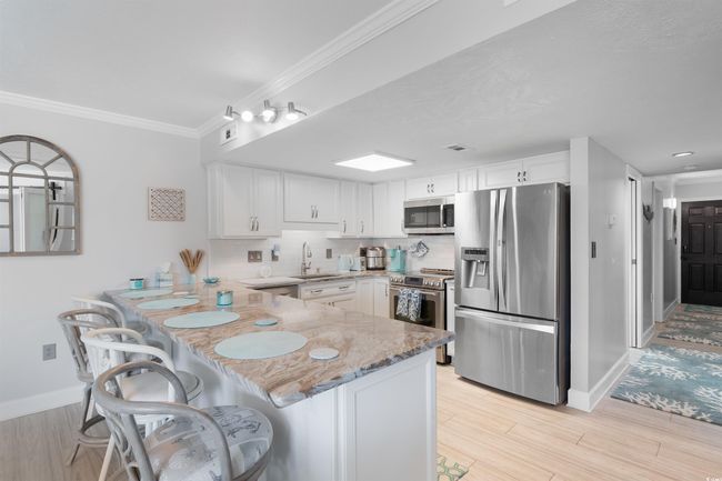 Kitchen featuring appliances with stainless steel finishes, a sink, a peninsula, white cabinets, and light stone counters | Image 6