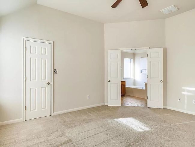 Unfurnished bedroom featuring light carpet, baseboards, connected bathroom, lofted ceiling, and ceiling fan | Image 17