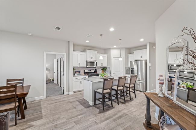 Kitchen with light wood finished floors, visible vents, an island with sink, a kitchen bar, and appliances with stainless steel finishes | Image 11