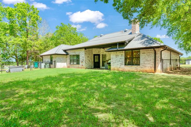 Back of property featuring a chimney, fence, a yard, brick siding, and metal roof | Image 21