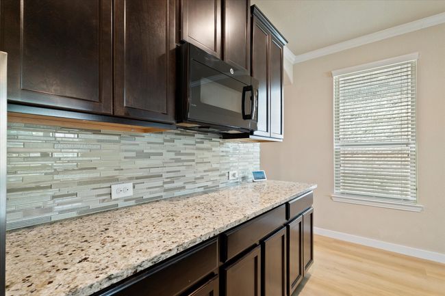 Kitchen with black microwave, crown molding, dark brown cabinetry, decorative backsplash, and baseboards | Image 33