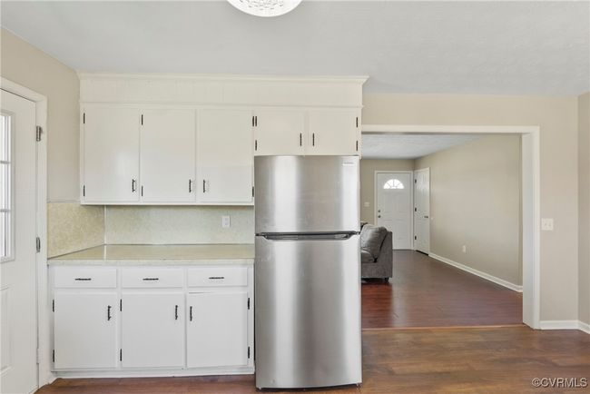 Kitchen with white cabinetry, light countertops, dark wood-style flooring, baseboards, and freestanding refrigerator | Image 7