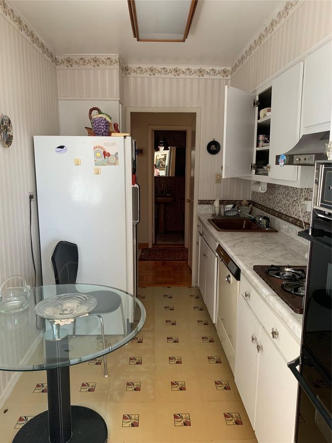 Kitchen with wallpapered walls, refrigerator, dishwashing machine, white cabinetry, and cooktop | Image 4