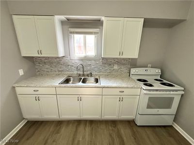 Kitchen featuring white cabinetry, backsplash, white electric stove, sink, and wood-type flooring | Image 2