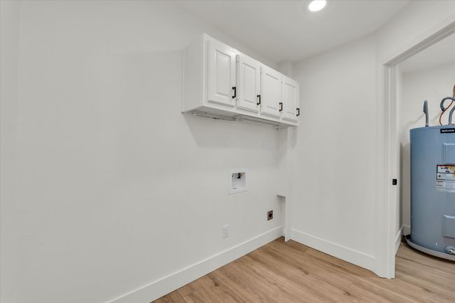 Clothes washing area with light wood-style floors, water heater, hookup for an electric dryer, washer hookup, and baseboards | Image 34