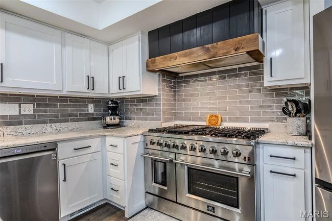 Kitchen featuring appliances with stainless steel finishes, custom exhaust hood, white cabinets, and tasteful backsplash | Image 22
