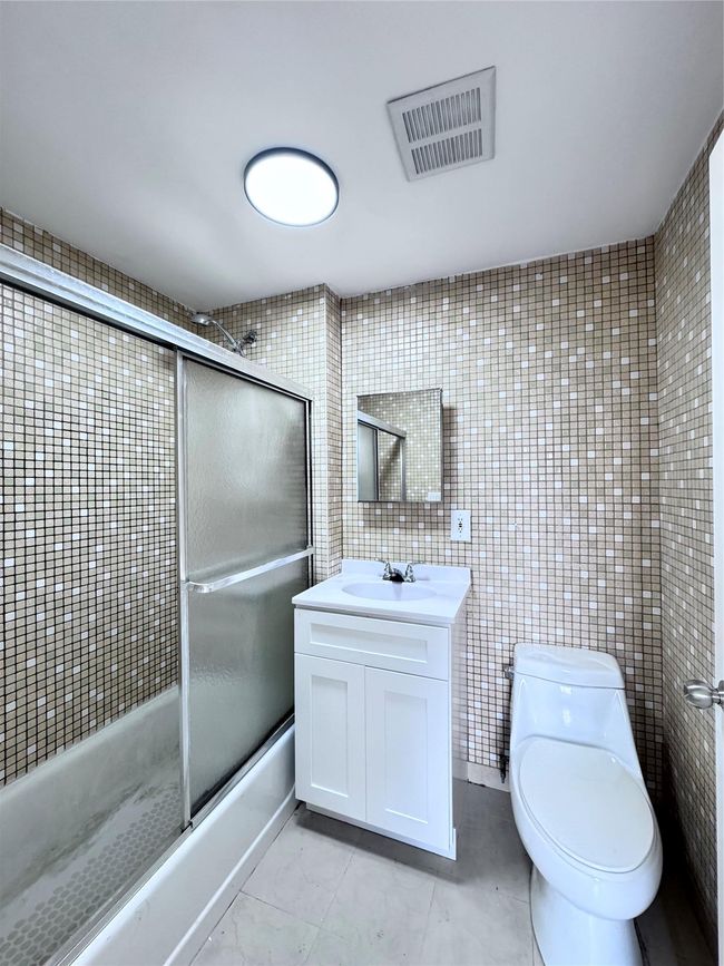 Bathroom with bath / shower combo with glass door, vanity, tile patterned floors, and tile walls | Image 8