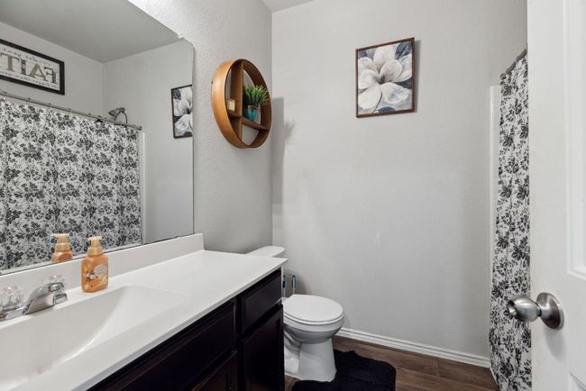 Bathroom with wood-vinyl finished floors, toilet, vanity, baseboards, and a shower with shower curtain | Image 12