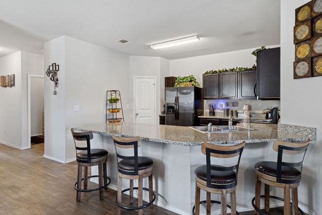 Kitchen with fridge with ice dispenser, a sink, dark brown cabinets, light stone counters, and wood-vinyl finished floors | Image 4