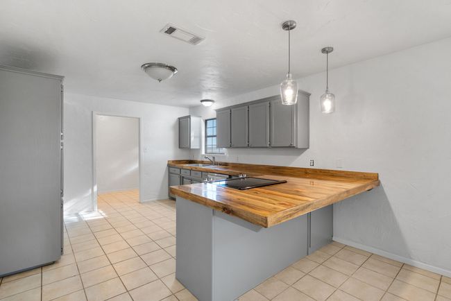 Kitchen with black electric cooktop, gray cabinets, a peninsula, light tile patterned flooring, and wood counters | Image 9