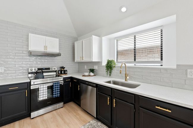 Kitchen featuring a sink, decorative backsplash, appliances with stainless steel finishes, white and dark cabinets, and under cabinet range hood | Image 14