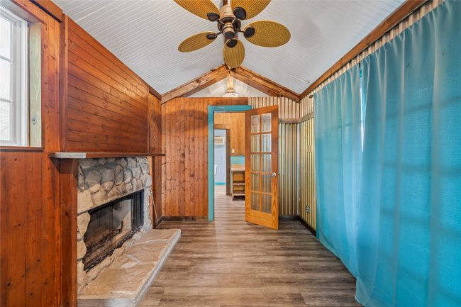 Unfurnished living room with lofted ceiling, a ceiling fan, wooden walls, a fireplace, and wood finished floors | Image 29