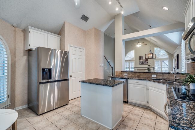 Kitchen with stainless steel appliances, lofted ceiling, white cabinetry, a sink, and dark stone countertops | Image 8