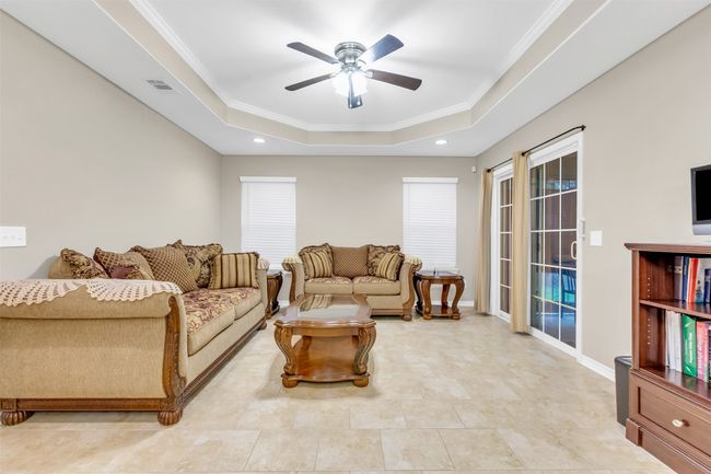 Living room with a raised ceiling, a ceiling fan, ornamental molding, and recessed lighting | Image 4
