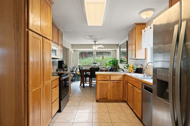 Kitchen featuring stainless steel appliances, a sink, a ceiling fan, light tile patterned floors, and brown cabinetry | Image 19