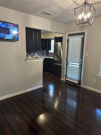 Kitchen with decorative light fixtures, dark hardwood / wood-style floors, backsplash, fridge, and a textured ceiling | Image 2