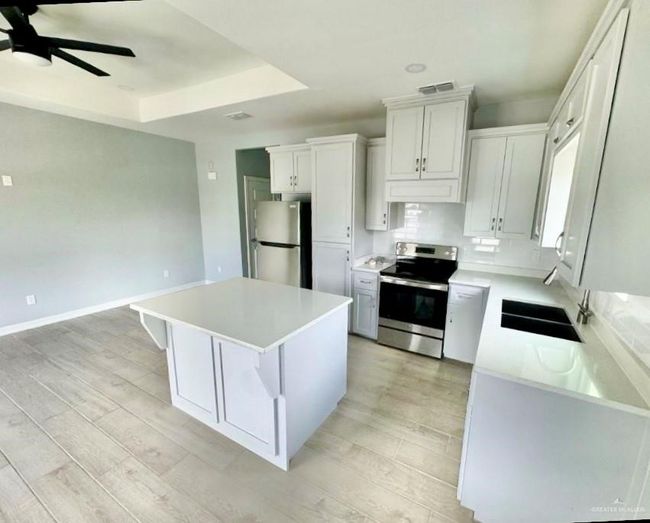 Kitchen with ceiling fan, stainless steel appliances, a kitchen island, white cabinets, and light countertops | Image 4