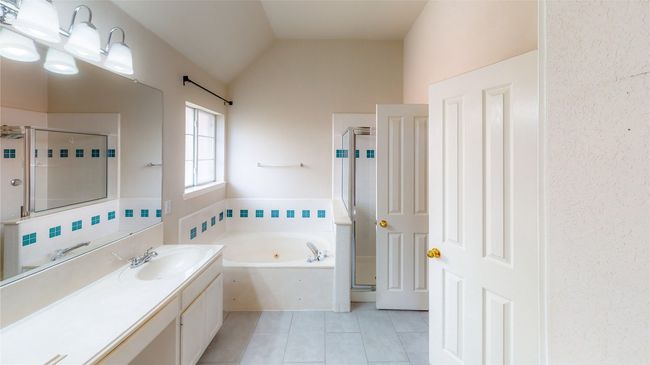 Full bathroom featuring a stall shower, a whirlpool tub, vanity, tile patterned floors, and lofted ceiling | Image 7