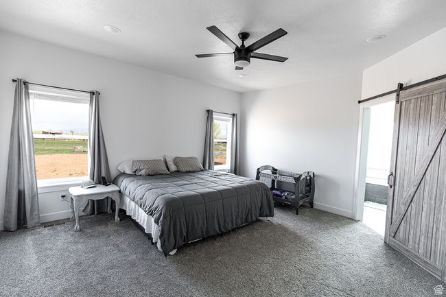 Carpeted bedroom with visible vents, a barn door, a ceiling fan, and multiple windows | Image 9