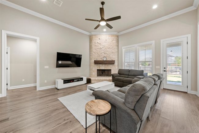 Living room with crown molding, light wood-style flooring, a ceiling fan, and a fireplace | Image 4