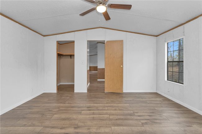 Unfurnished bedroom with lofted ceiling, wood finished floors, ornamental molding, and a ceiling fan | Image 14
