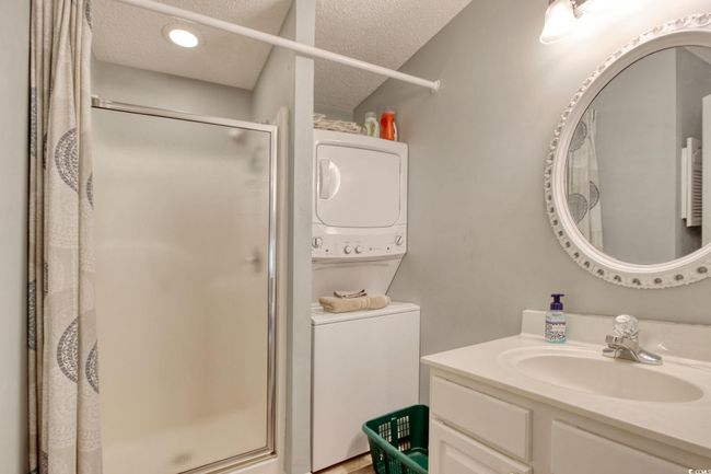 Full bath featuring stacked washer / drying machine, a stall shower, a textured ceiling, and vanity | Image 27