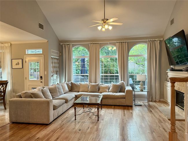 Living room with visible vents, wood finished floors, a stone fireplace, high vaulted ceiling, and a ceiling fan | Image 15