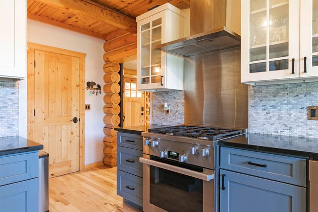 Kitchen featuring stainless steel gas stove, ventilation hood, log walls, decorative backsplash, and light solid wood-style flooring | Image 9