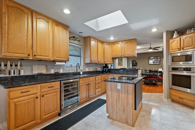 Kitchen featuring stainless steel appliances, beverage cooler, a sink, a skylight, and dark stone counters | Image 14