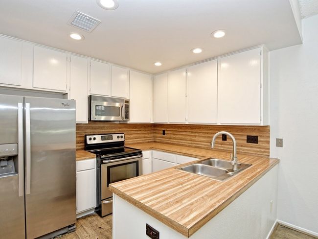 Kitchen with tasteful backsplash, appliances with stainless steel finishes, white cabinets, a sink, and visible vents | Image 6