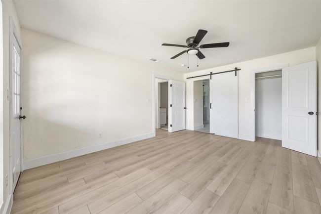 Unfurnished bedroom with a barn door, light wood-style floors, a ceiling fan, and ensuite bath | Image 36