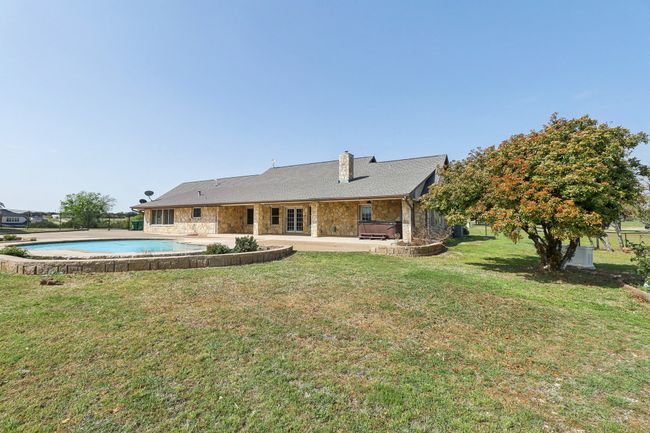 Rear view of property featuring stone siding, a patio area, a chimney, an outdoor pool, and a yard | Image 30