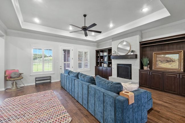Living room featuring a raised ceiling, a ceiling fan, a fireplace, dark wood finished floors, and ornamental molding | Image 10