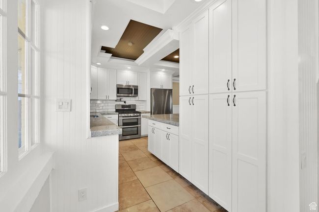 Kitchen featuring tasteful backsplash, crown molding, light tile patterned flooring, white cabinetry, and appliances with stainless steel finishes | Image 10