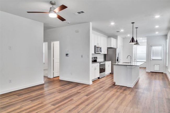 Kitchen featuring stainless steel appliances, visible vents, white cabinets, a sink, and wood finished floors | Image 5