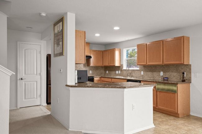 Kitchen with tasteful backsplash, freestanding refrigerator, dark stone counters, a peninsula, and under cabinet range hood | Image 6