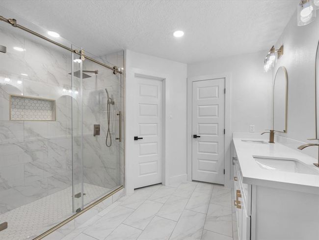 This bathroom features a spacious glass-enclosed shower with marble-style tiles and a built-in niche. It includes a double vanity with modern fixtures, sleek white cabinetry, and elegant lighting, creating a bright and contemporary space. | Image 22
