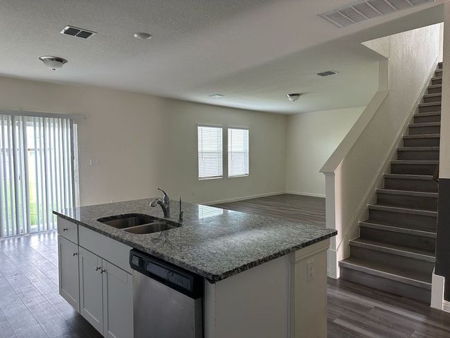 Kitchen with dishwasher, dark wood finished floors, dark stone countertops, a center island with sink, and a textured ceiling | Image 22