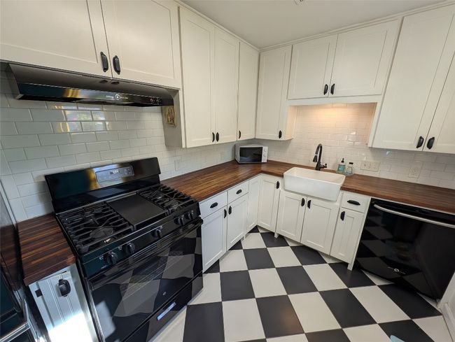 Kitchen with wood counters, under cabinet range hood, a sink, and black appliances | Image 4