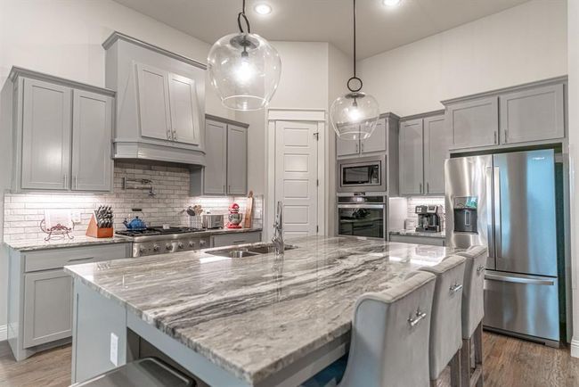 Kitchen with light wood-type flooring, premium range hood, stainless steel gas stovetop, decorative light fixtures, and tasteful backsplash | Image 12