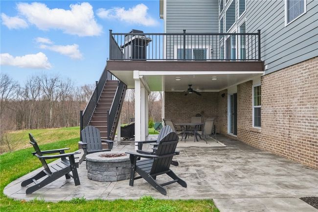 Beautifully designed outdoor living space featuring a covered patio with ceiling fan, an upper-level composite deck with stairs, and a cozy stamped concrete fire pit area. Perfect for relaxing or entertaining, all set against a peaceful wooded backdrop. | Image 35