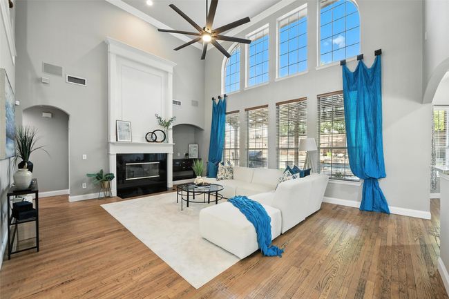 Living room with arched walkways, wood finished floors, a fireplace with flush hearth, crown molding, and a high ceiling | Image 7