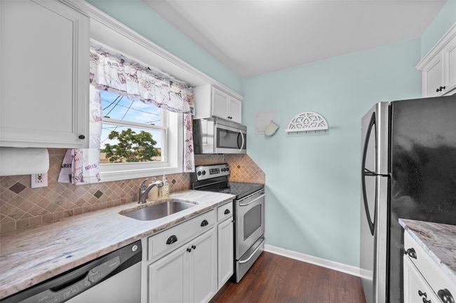 Kitchen with appliances with stainless steel finishes, decorative backsplash, light stone counters, dark wood finished floors, and white cabinets | Image 14