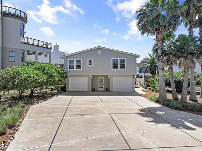 This is a charming two-story home with a modern design, featuring a large driveway leading to two garages. It's surrounded by lush greenery and tall palm trees, offering a serene and inviting atmosphere. | Image 30