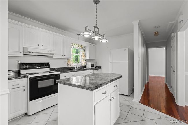 Kitchen with a center island, under cabinet range hood, white appliances, white cabinets, and ornamental molding | Image 10