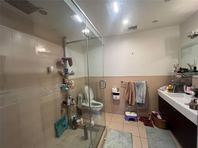 Bathroom with tile walls, a shower stall, tile patterned floors, toilet, and visible vents | Image 12