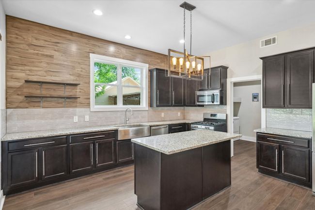 Kitchen with appliances with stainless steel finishes, a sink, a chandelier, light stone countertops, and decorative backsplash | Image 9