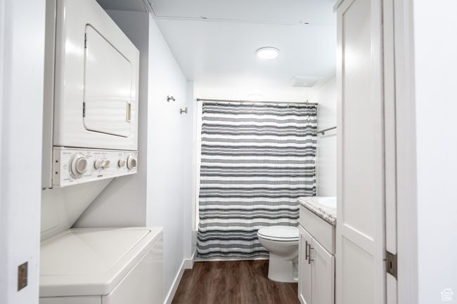 Bathroom featuring stacked washer / dryer, baseboards, toilet, wood finished floors, and vanity | Image 10
