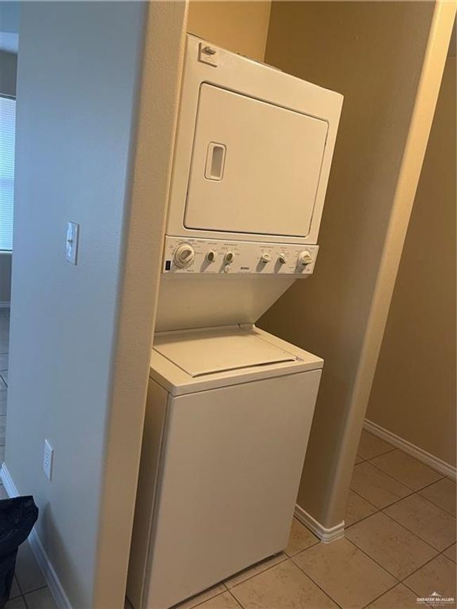 Washroom with stacked washing machine and dryer, light tile patterned floors, and baseboards | Image 4